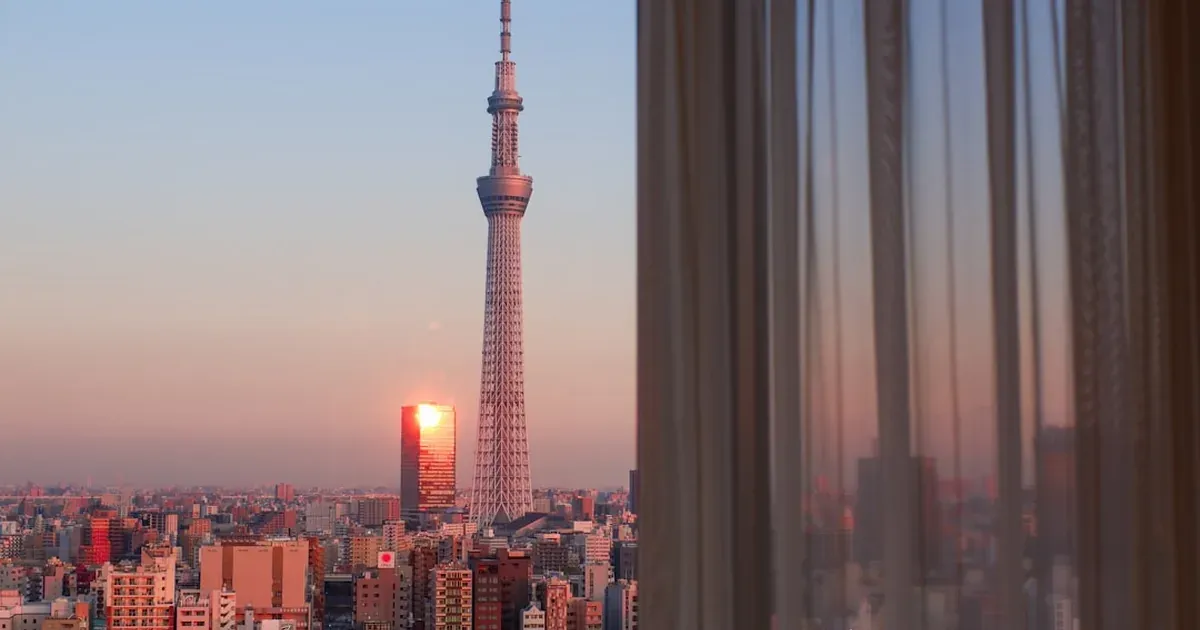 A modern Japanese hotel room with a clean bed, soft lighting, and a Tokyo city view at night