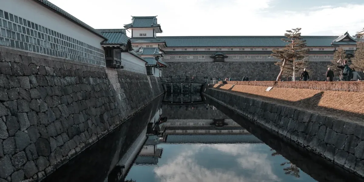 Kanazawa Castle Park with stone walls, traditional Japanese castle keep, and moat with autumn trees reflected in the water