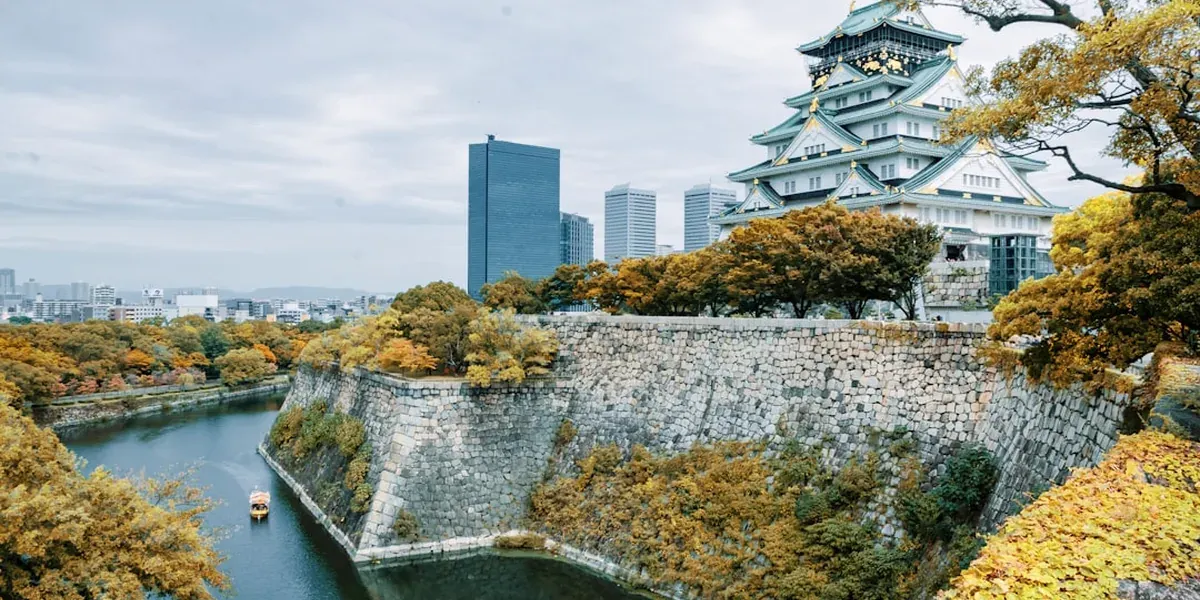Osaka Castle surrounded by vibrant red and orange autumn maple trees in a large park